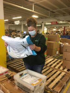 An eFulfillment Service employee is shown working in the warehouse, masked and reading the label on a package she's holding.