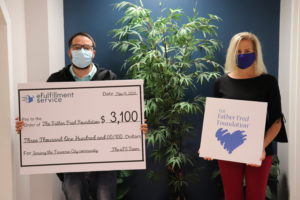 Mike Claycomb, eFS Warehouse Manager, stands on the right holding a large check representing the eFS donation to The Father Fred Foundation. To the right Elaine Talue, Advancement Manager of Father Fred, stands holding The Father Fred Foundation logo. Both are wearing face masks.