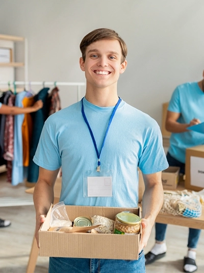 male in blue shirt holding a box of goods while helping a non profit business