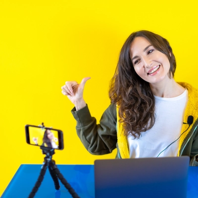 Female Content Creator in front of yellow background wearing a green and yellow hoodie.