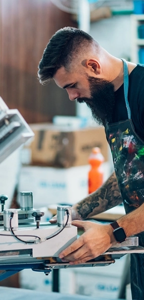 Bearded man wearing an apron screen printing a t-shirt for merchandise