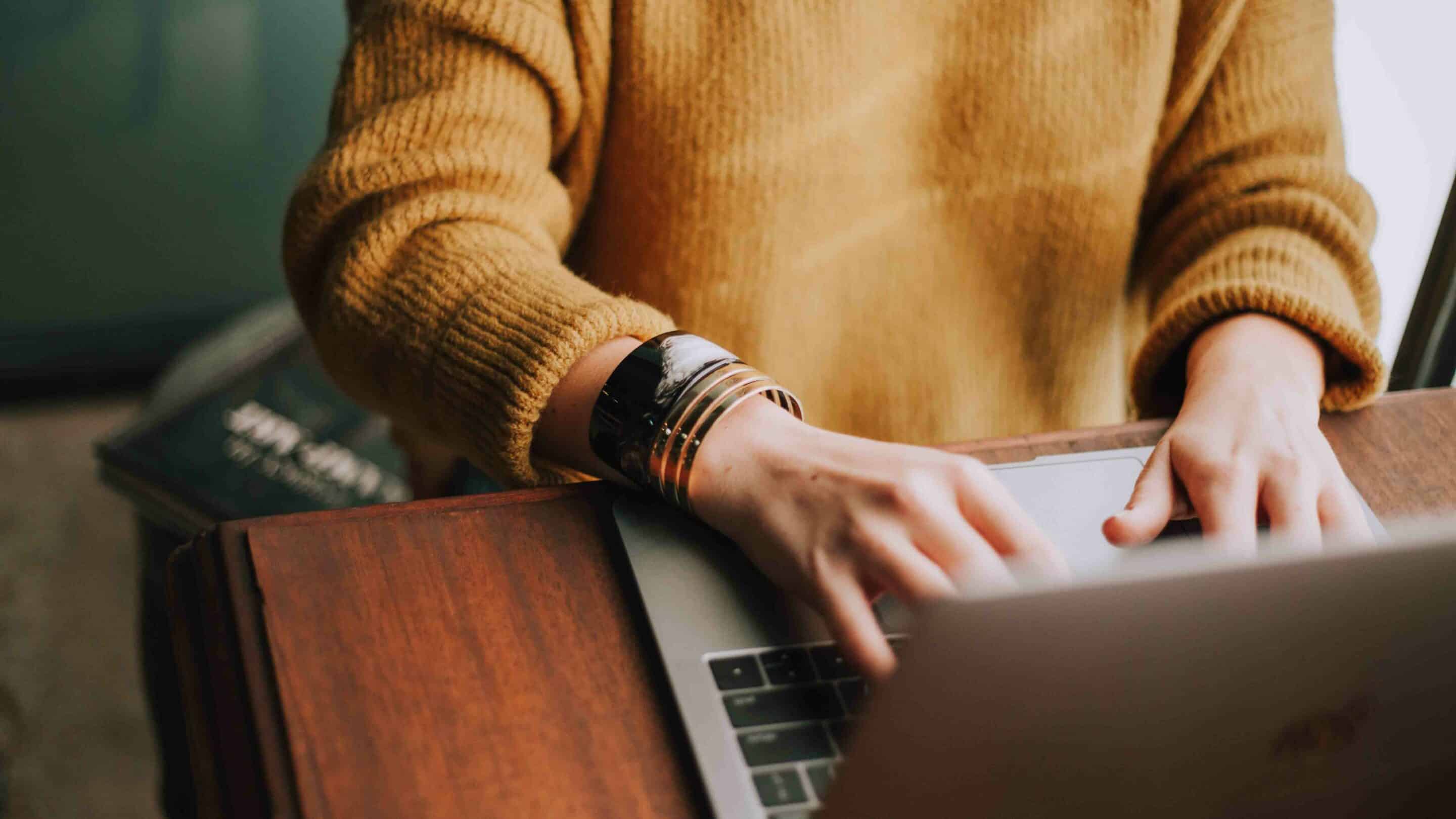 person in yellow sweater typing on computer