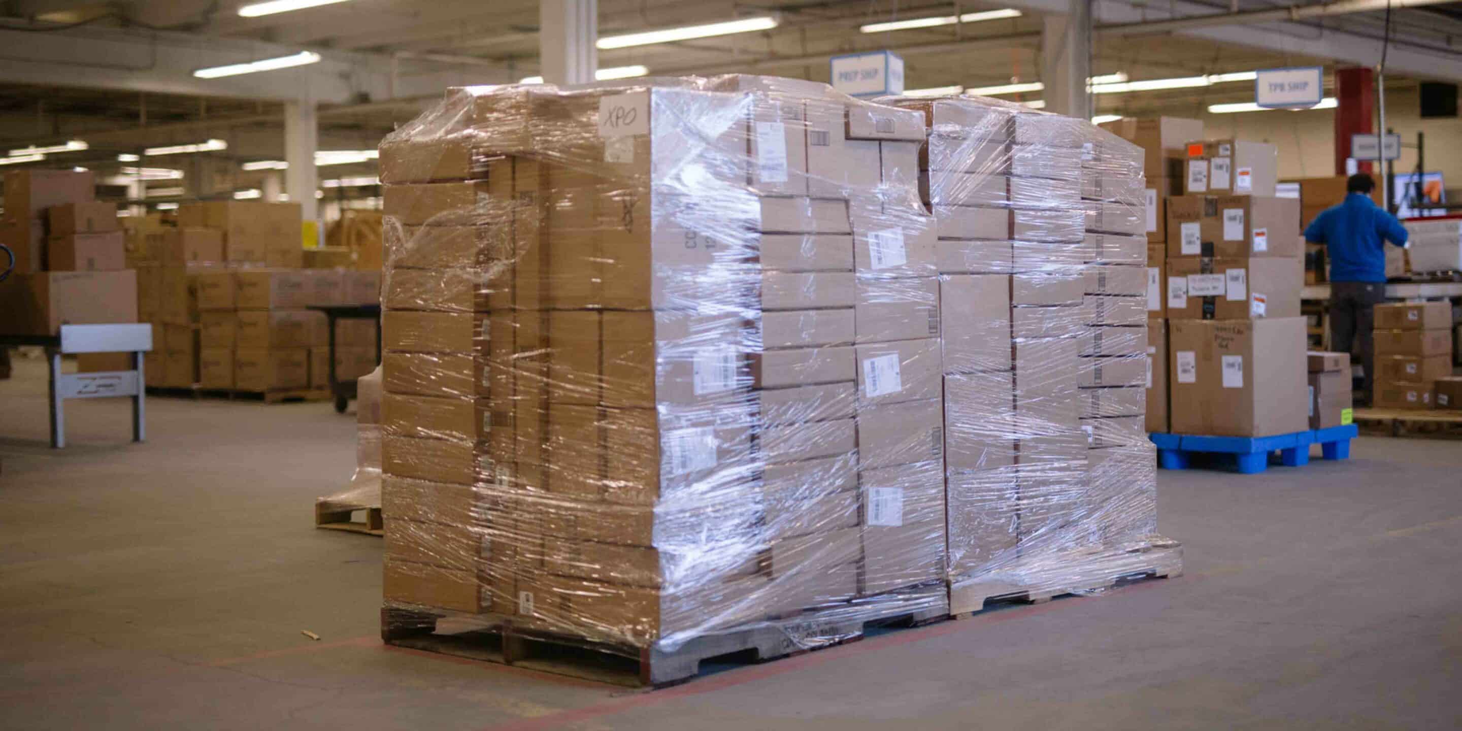 picture of a women warehouse worker holding a box among many shelves in a warehouse