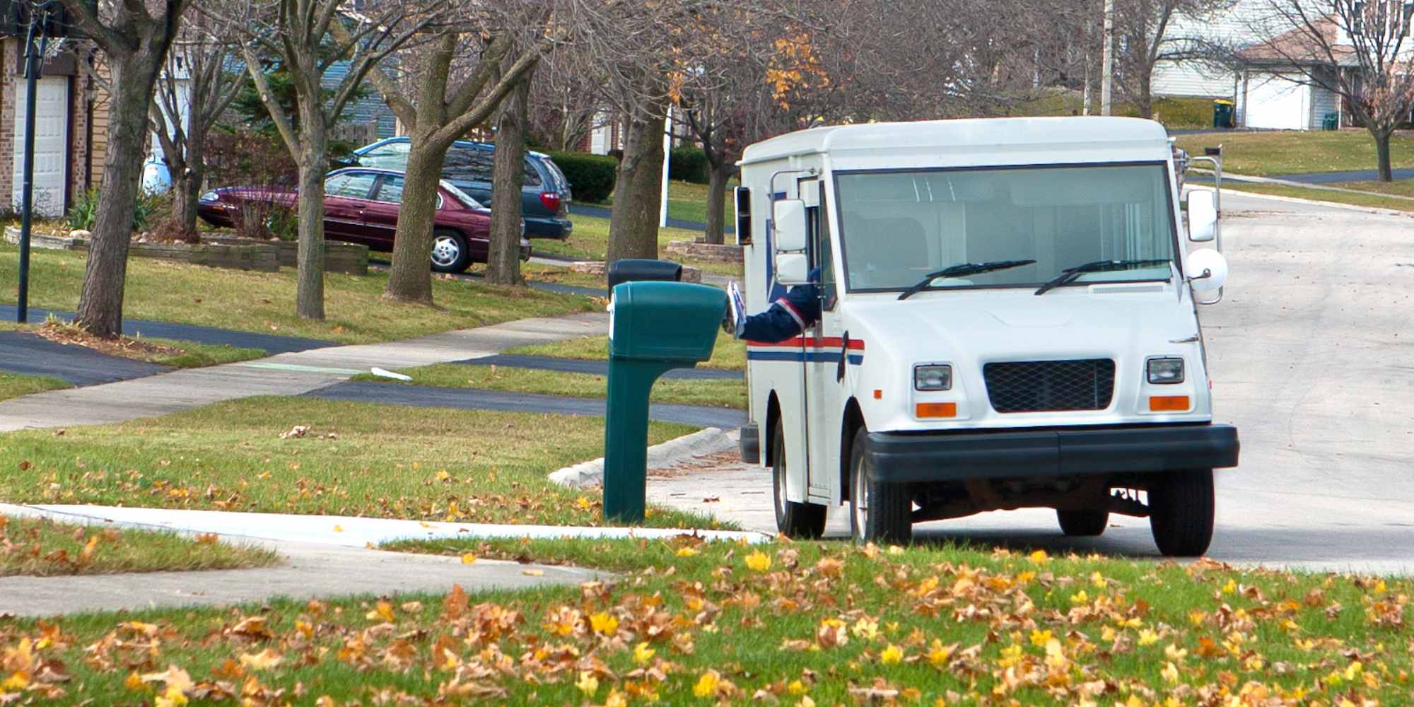 Photo of a white mail truck delivering a package in a neighborhood